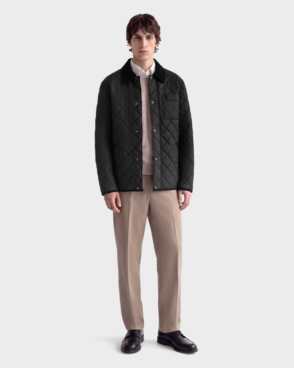 A man wearing a black Rudsak MONTY - 6126722 Black quilted jacket with a collar, a beige sweater, a collared shirt, tan trousers, and black loafers.