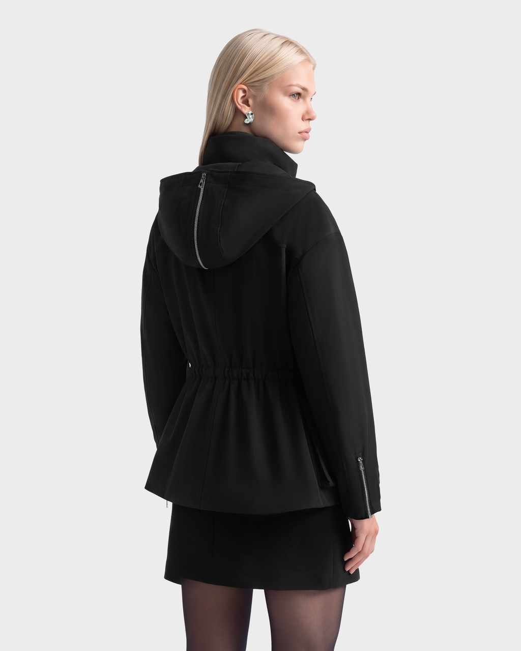 A woman seen from behind wearing a black Rudsak ROSALINDA - 8126523 insulated hooded jacket with a cinched waist and silver zippers on the hood and cuffs.