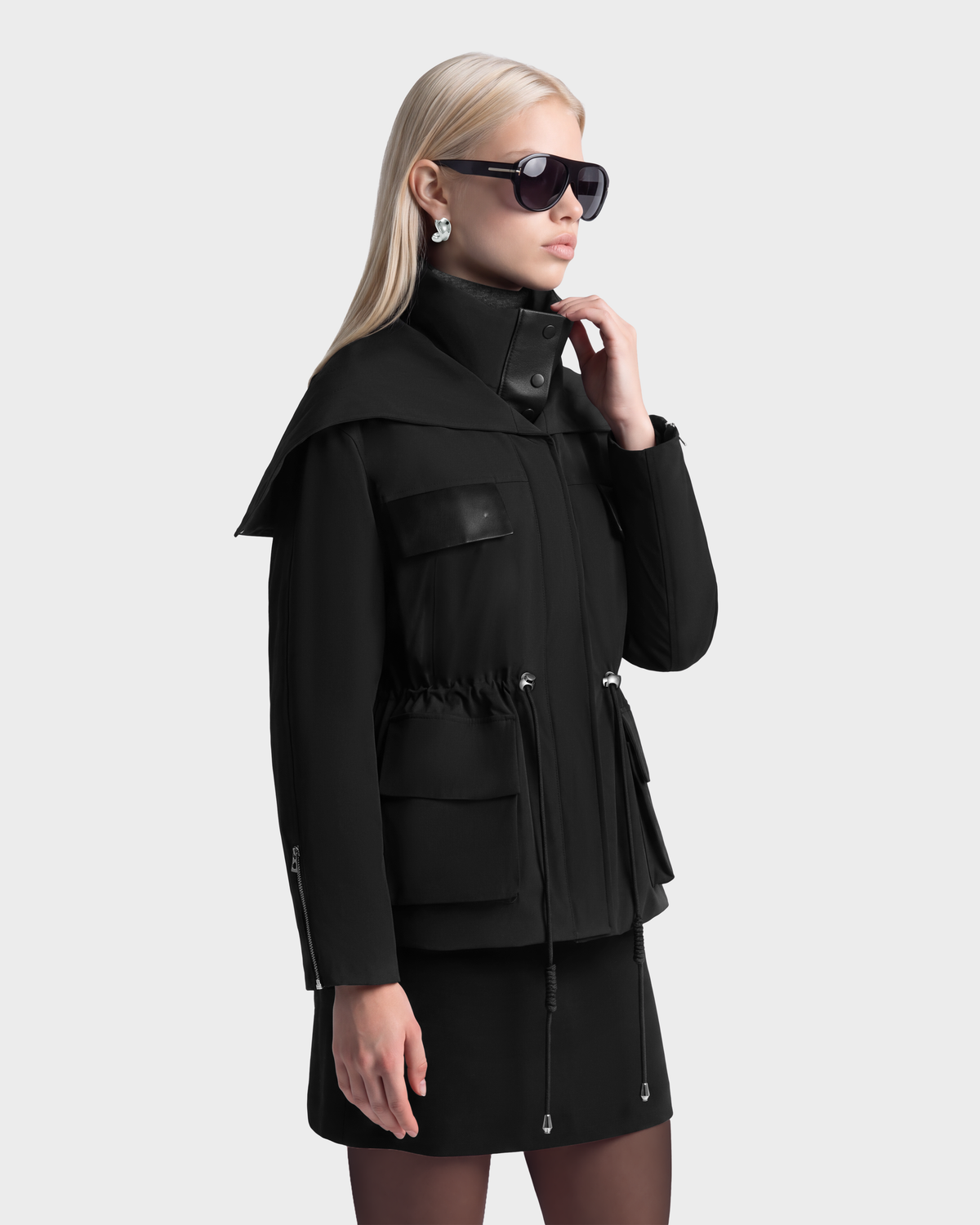 A person in profile wears a black ROSALINDA - 8126523 Rudsak duck down winter coat with a high collar, utility pockets, and a drawstring waist.