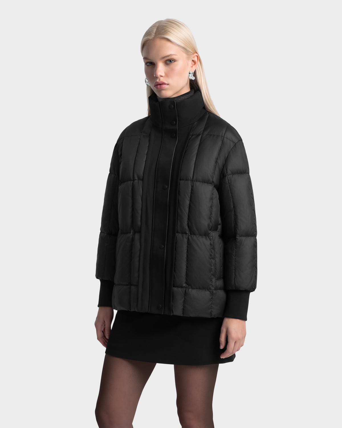 A model wearing a black, boxy-fit ROSALINDA - 8126523 Black insulated puffer jacket with a high collar, snap buttons, and ribbed cuffs.