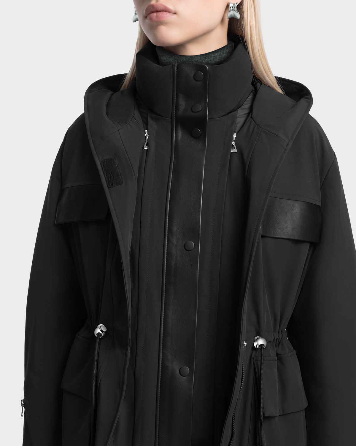 A person wearing a black Rudsak ROSALINDA - 8126523 insulated hooded parka with a high collar, snap-button placket, and drawstring waist.