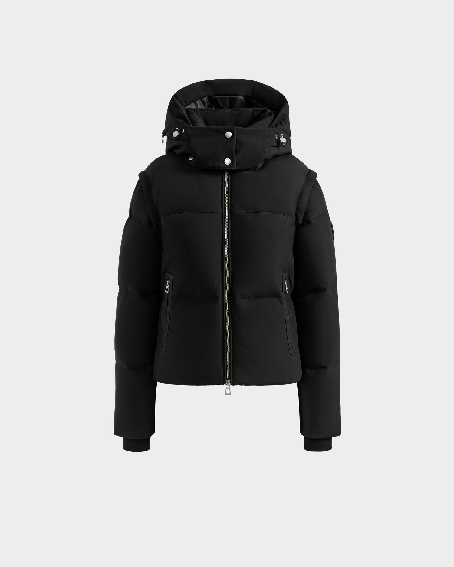 The DELILAH M - L125538 Black by Rudsak is a women's black hooded down puffer jacket with a front zipper, side zip pockets, and button details on the hood, shown against a plain light gray background.