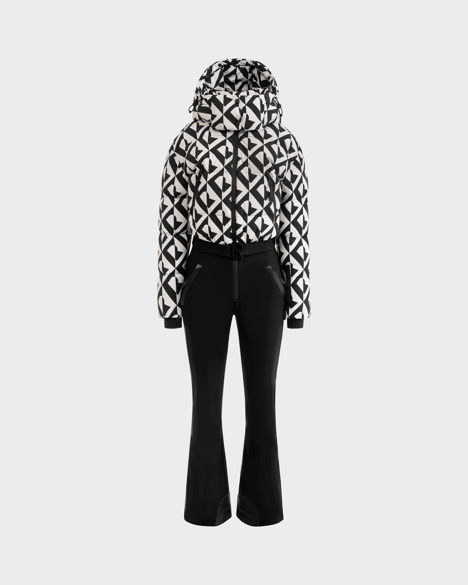 The Rudsak DINARA - 8125600 Vanilla Monogram women’s ski suit with a black and white geometric pattern and hood is shown with fitted black ski pants on a plain light background.
