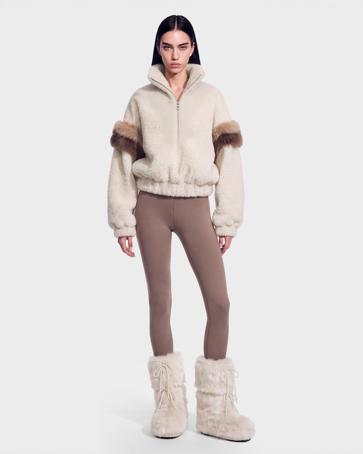 A person stands facing forward wearing the ALEIA - 8526693 Vanilla cream fleece jacket by Rudsak, featuring brown furry accents, paired with taupe leggings and cream furry boots against a plain white background.