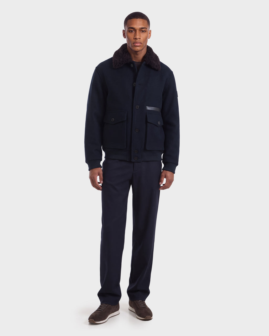 A man wearing the JULIUS - 6126723 Navy jacket with a dark faux-fur collar, navy trousers, and dark sneakers.