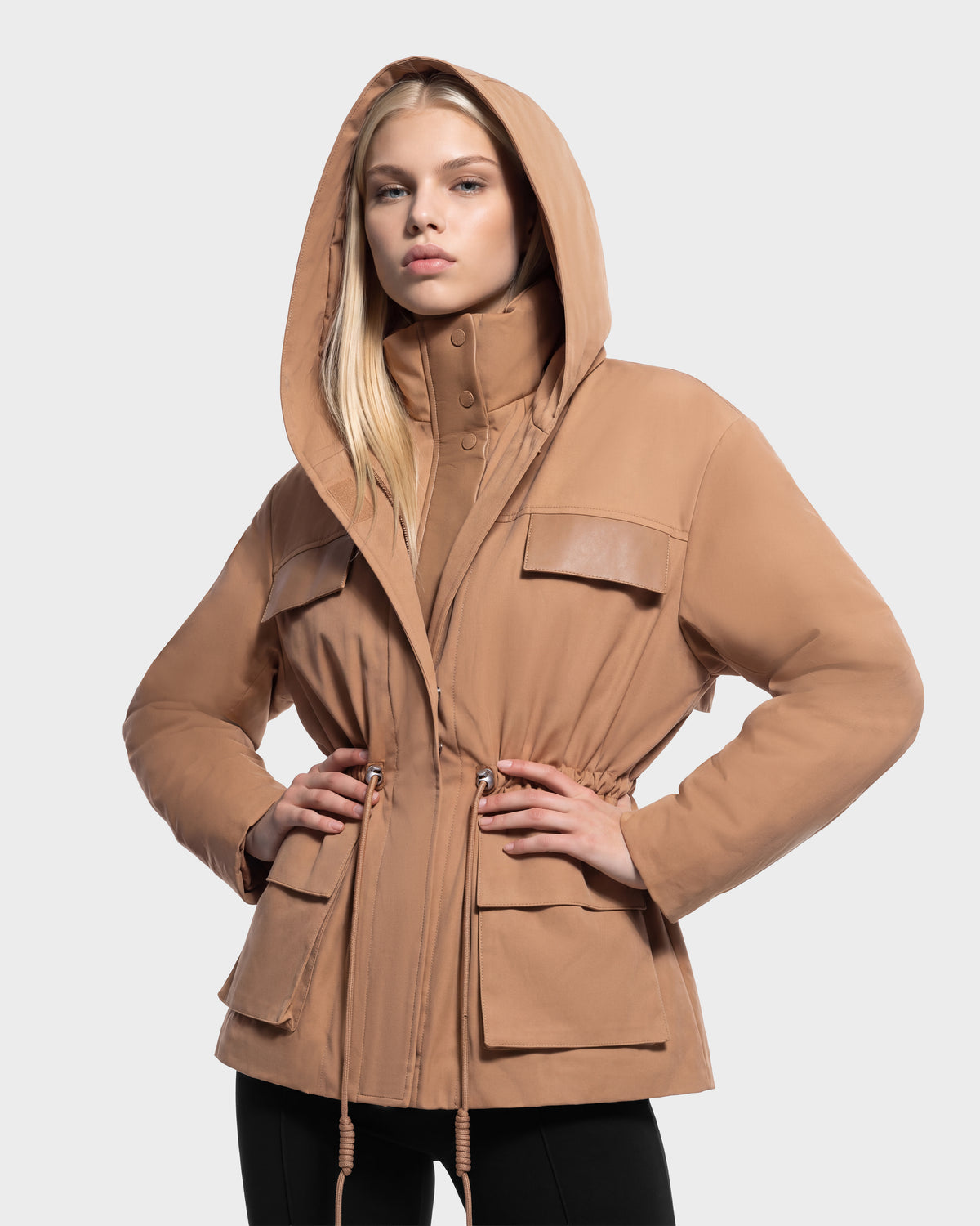 A person wearing a ROSALINDA - 8126523 Camel hooded jacket in camel, featuring front flap pockets and a drawstring waist.