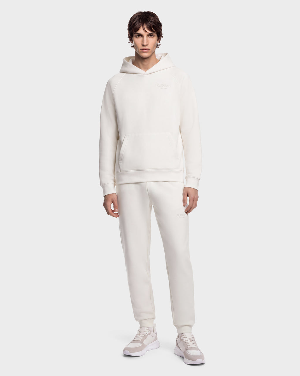 A person wears the BRIAR - 9525001 Vanilla M matching cream-colored hooded sweatshirt and sweatpants with white sneakers.