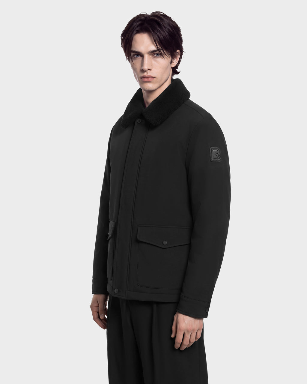 A man wearing a black ANTOINE - 6126506 Rudsak utility jacket with a faux-fur collar and large front pockets.