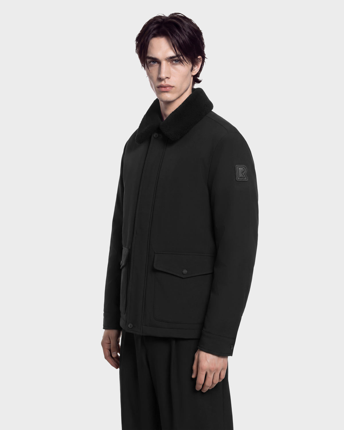 A man wearing a black ANTOINE - 6126506 Rudsak utility jacket with a faux-fur collar and large front pockets.