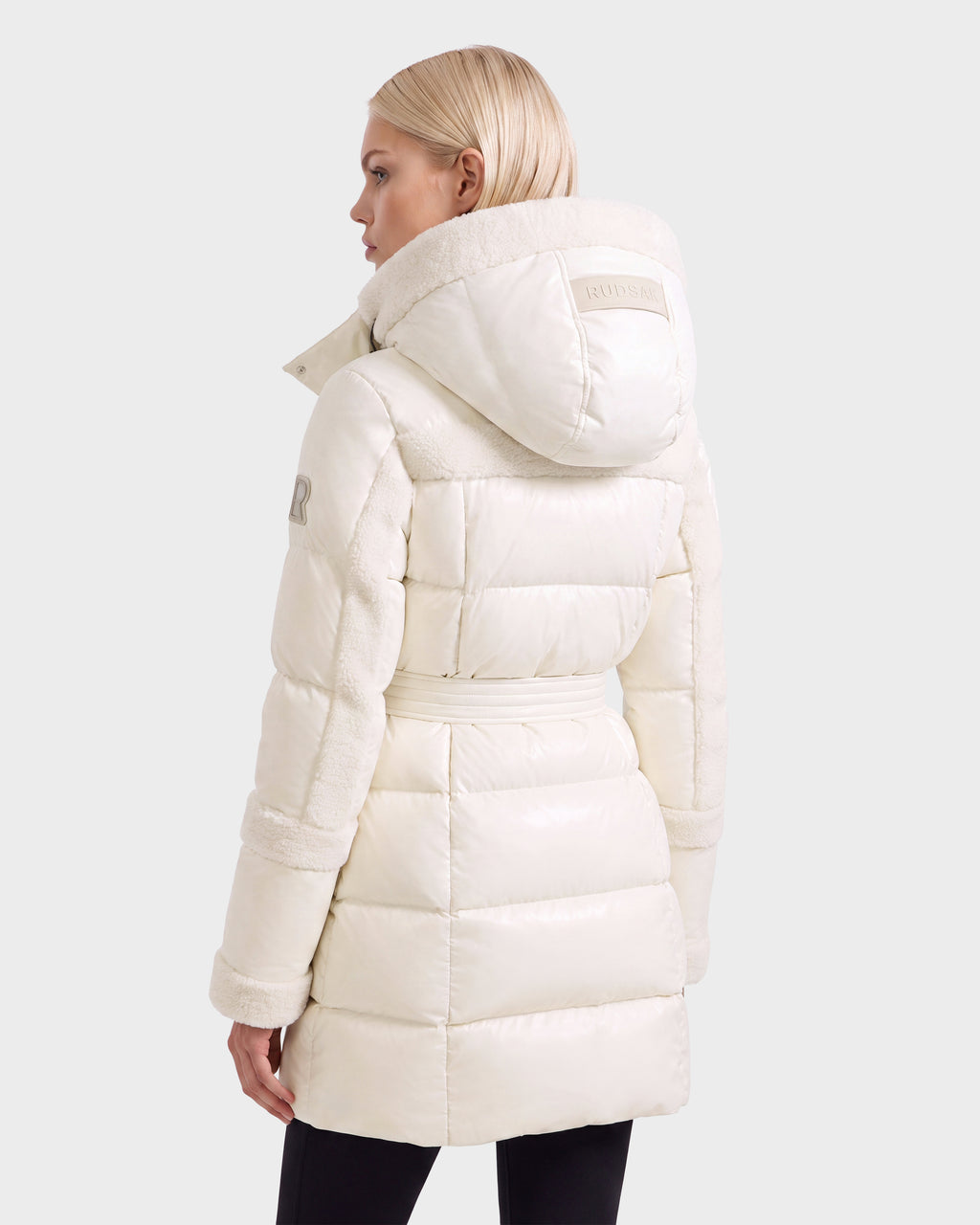 A woman seen from the back wearing a knee-length, cream-colored, hooded Rudsak AUDREY L - 8124585 Vanilla belted puffer coat with faux-fur trim.