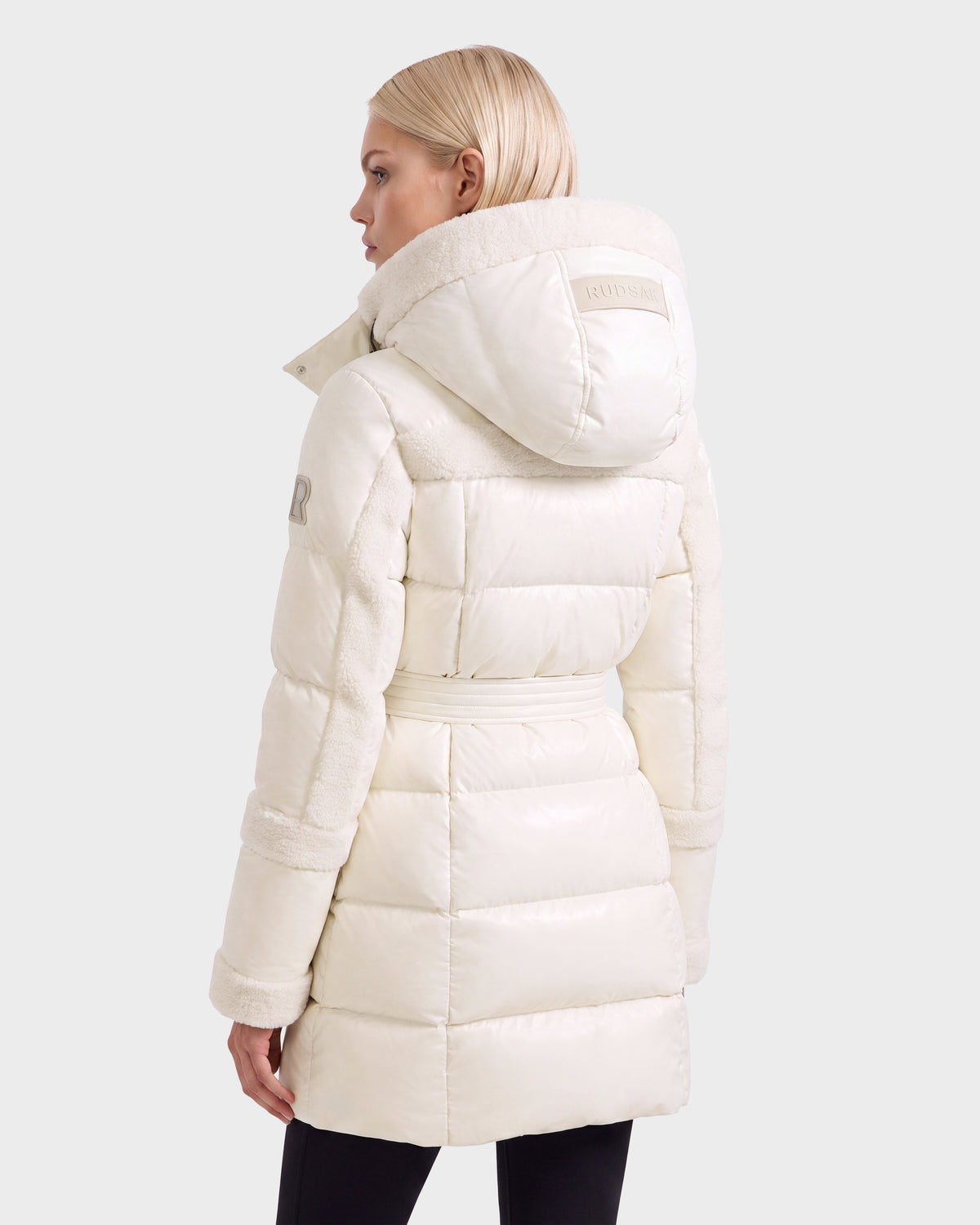 A woman seen from the back wearing a knee-length, cream-colored, hooded Rudsak AUDREY L - 8124585 Vanilla belted puffer coat with faux-fur trim.