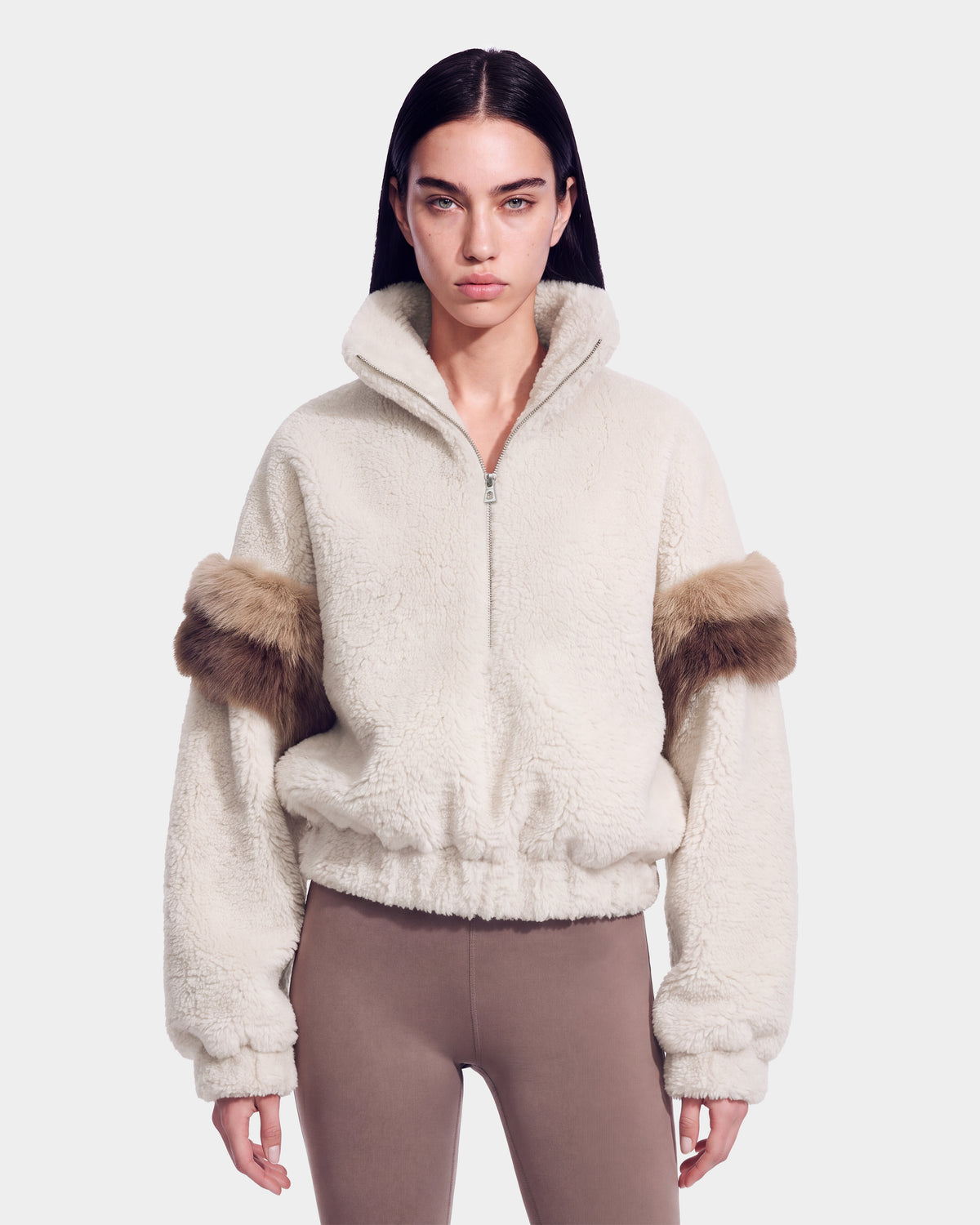 A woman wearing the Rudsak ALEIA - 8526693 Vanilla textured cream zip-up jacket with brown fur sleeve accents and taupe leggings, standing against a plain light background.