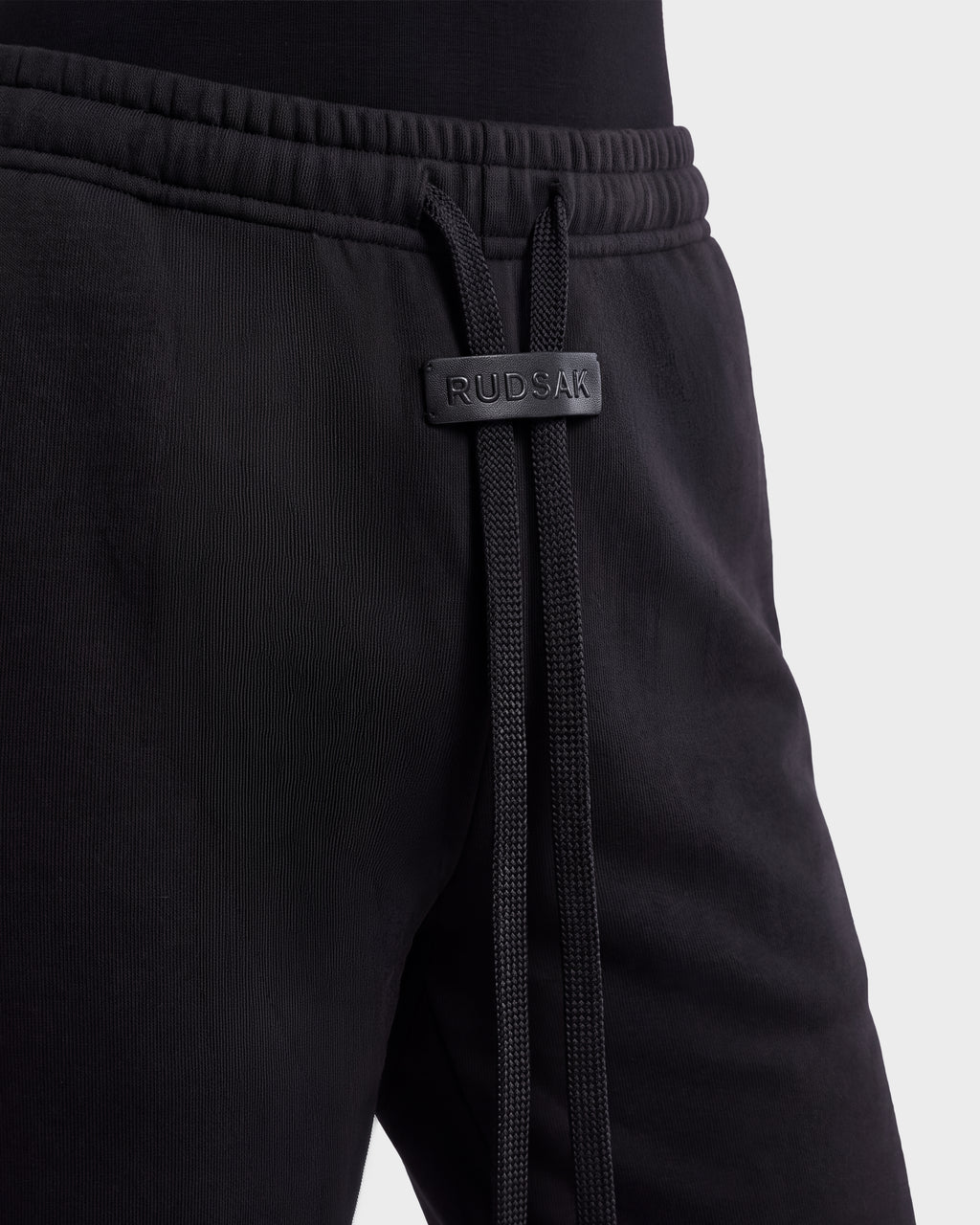 Close-up of ANGEL - 8526725 Black contemporary sweatpants with a drawstring waist featuring a branded leather tab.