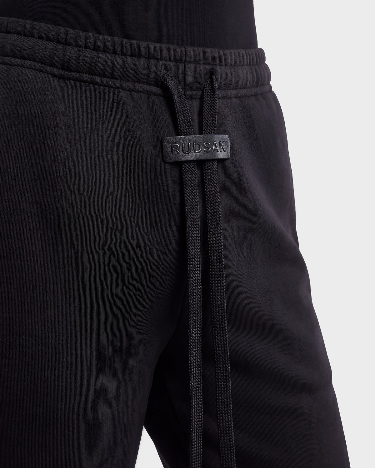 Close-up of ANGEL - 8526725 Black contemporary sweatpants with a drawstring waist featuring a branded leather tab.