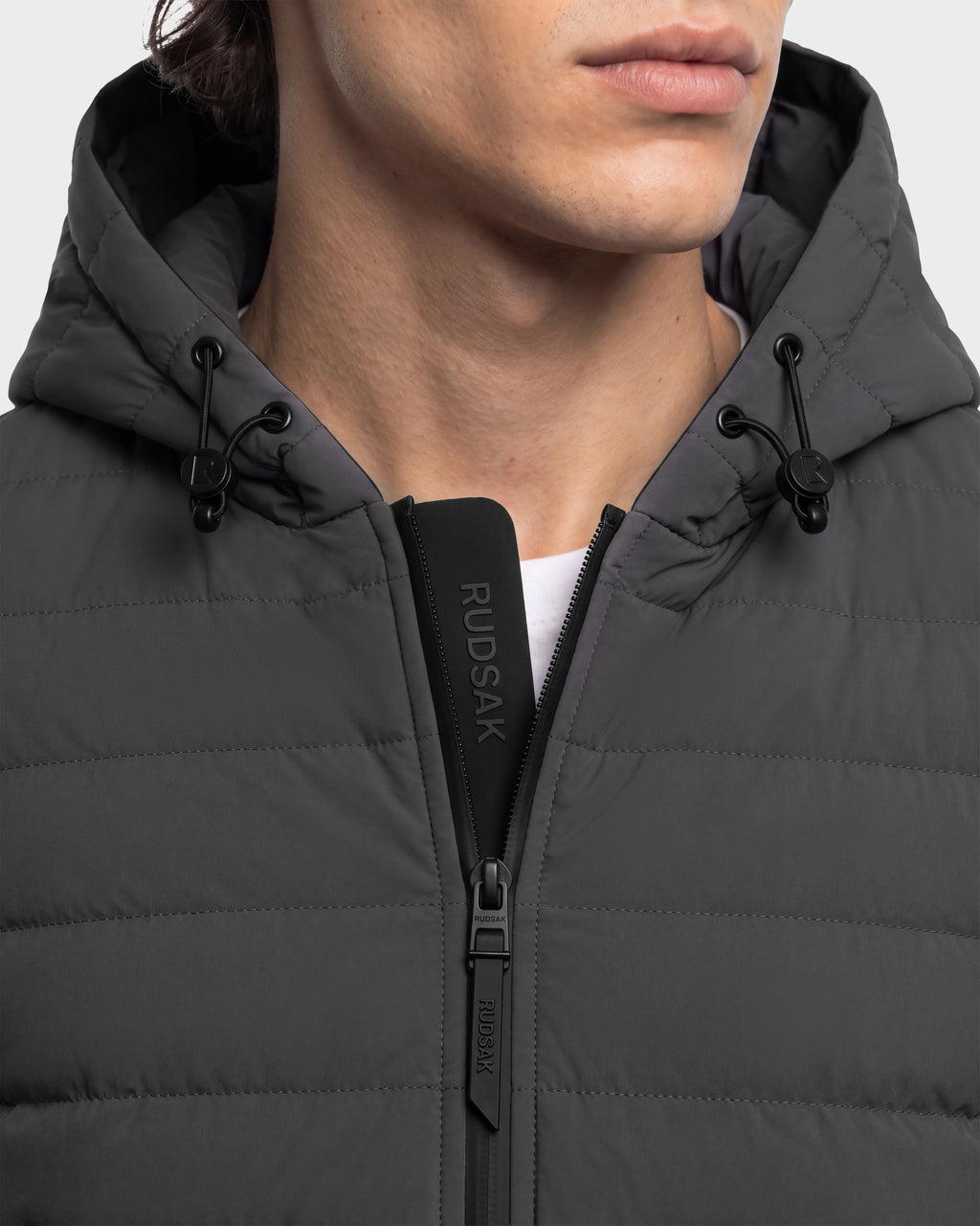 Close-up of a person wearing a grey Rudsak DEE MAT - 6124028 quilted lightweight hybrid down jacket with a black zipper and drawstring hood.