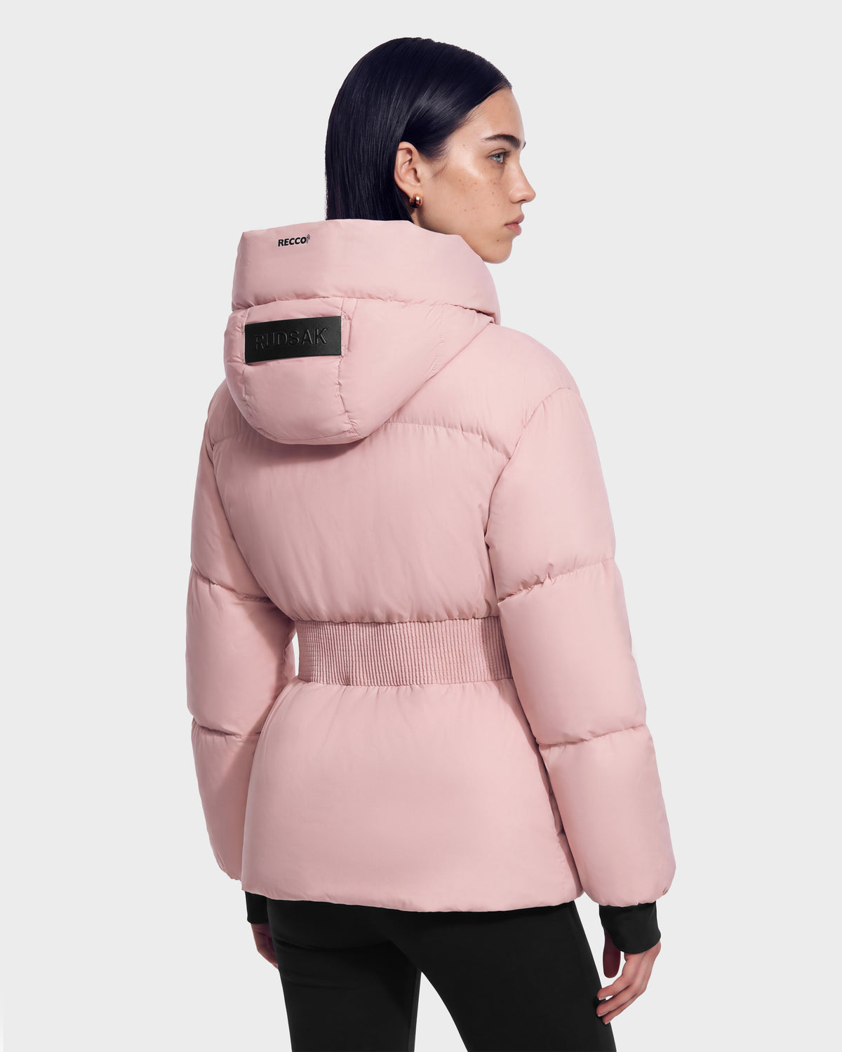 A person viewed from behind wearing a Rudsak DIAMOND - 8126772 Vintage Rose light pink quilted puffer with a cinched elastic waist.