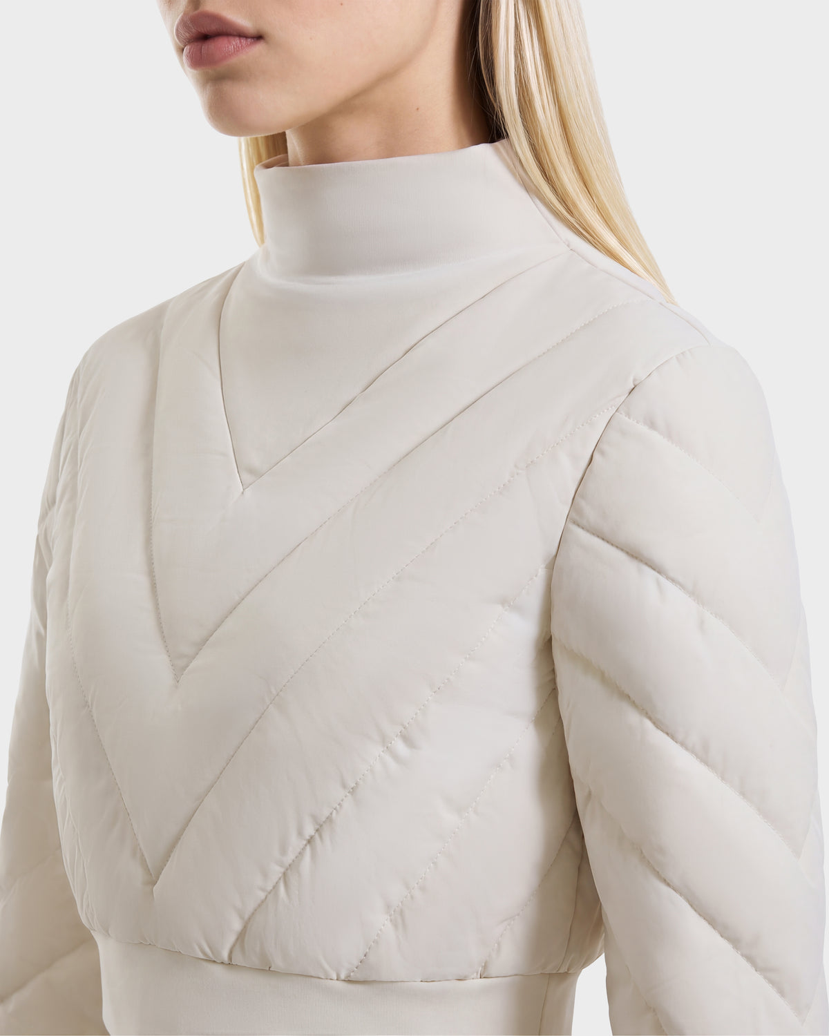 A cream-colored KATYA - 8526531 Vanilla cropped down sweatshirt featuring a mock-neck and a quilted chevron pattern on the bodice.