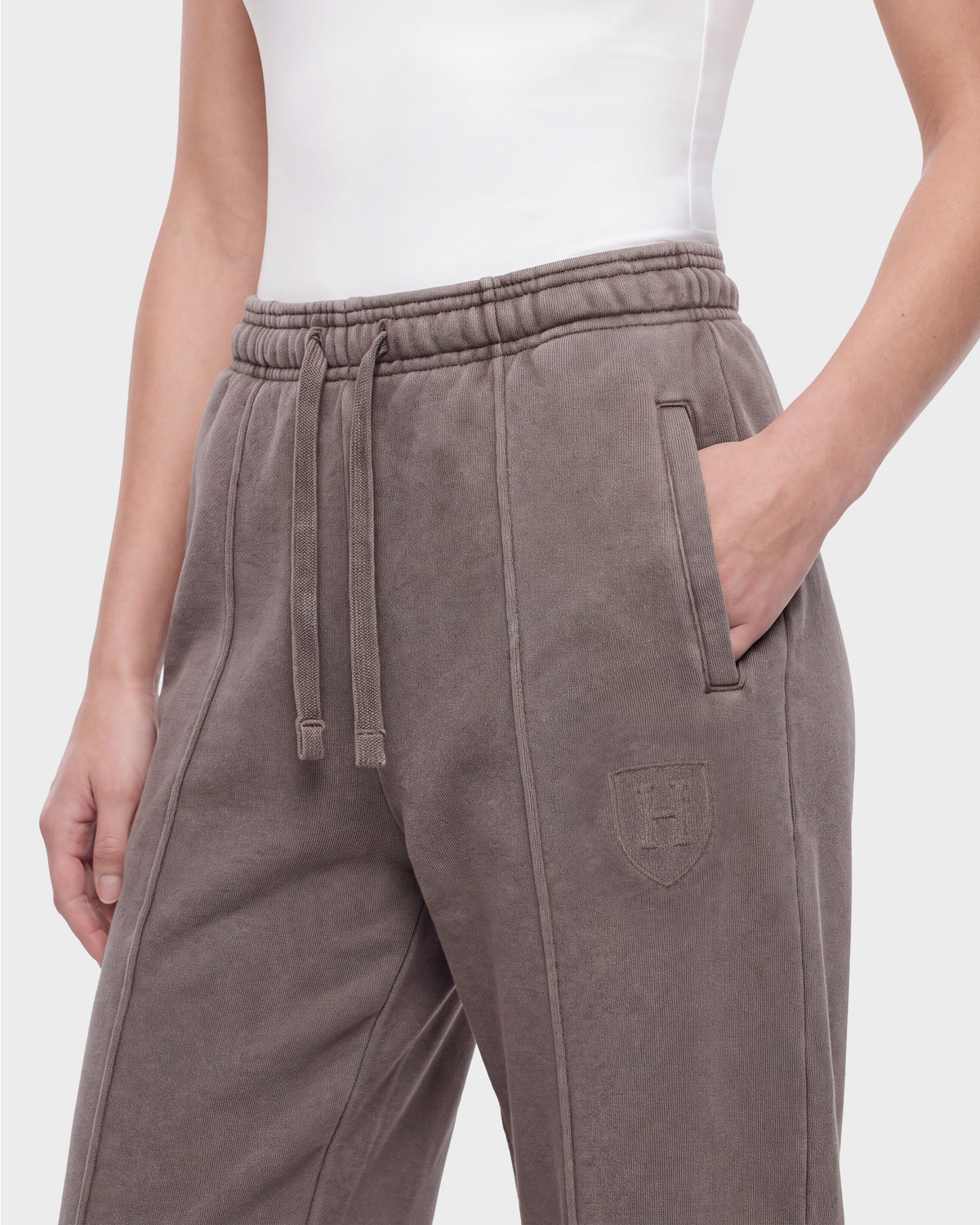 A person wearing the Rudsak GAELLE HV - H526902 Taupe heavyweight jersey jogger sweatpants, featuring an elastic waistband, drawstring, and a crest logo on the left thigh. One hand is in the pocket.