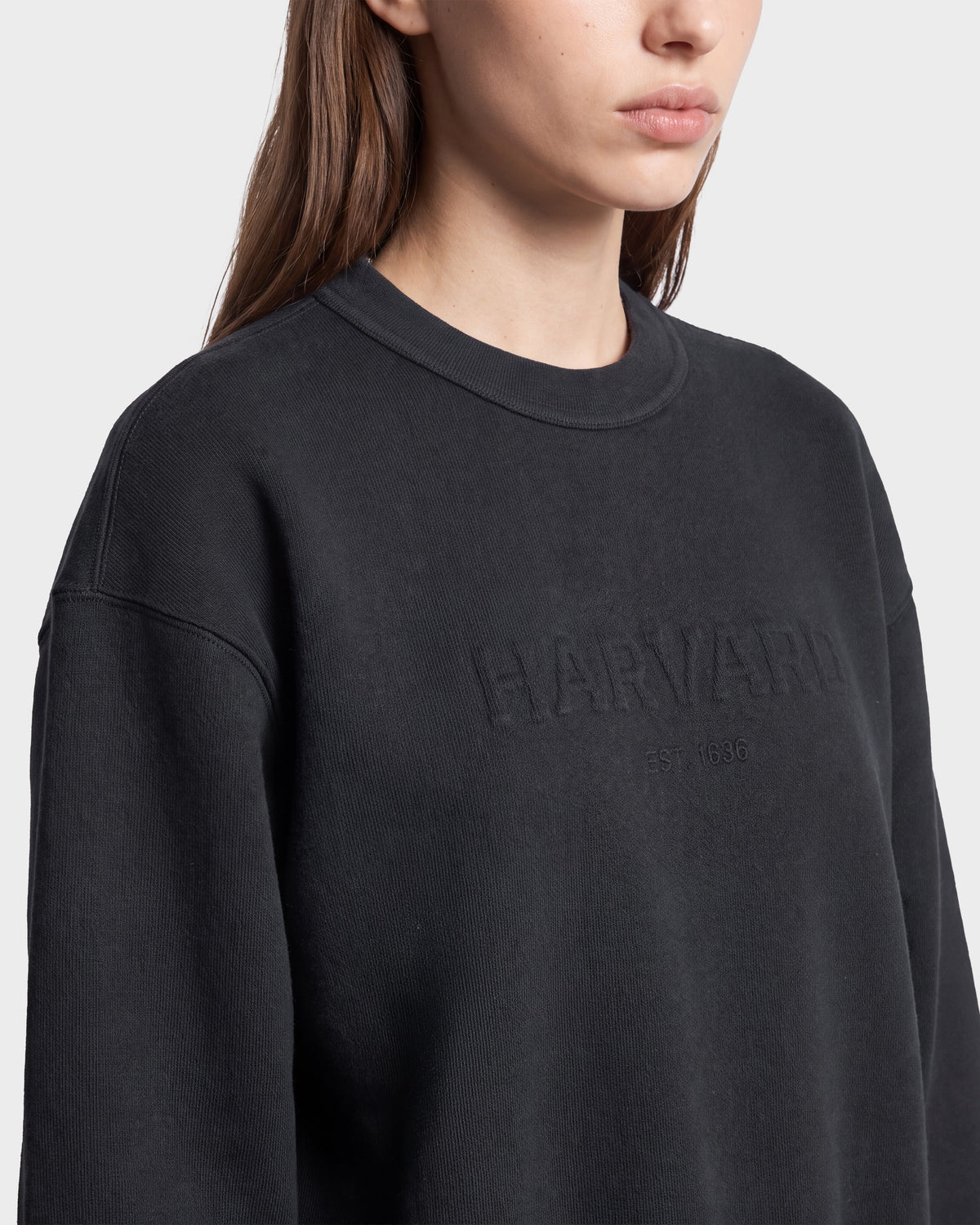 A person wearing a Rudsak LEXYE HV - H526900 Titanium sweatshirt with “HARVARD” and “EST. 1636” embossed on the front. Only the lower half of the face and upper body are visible.