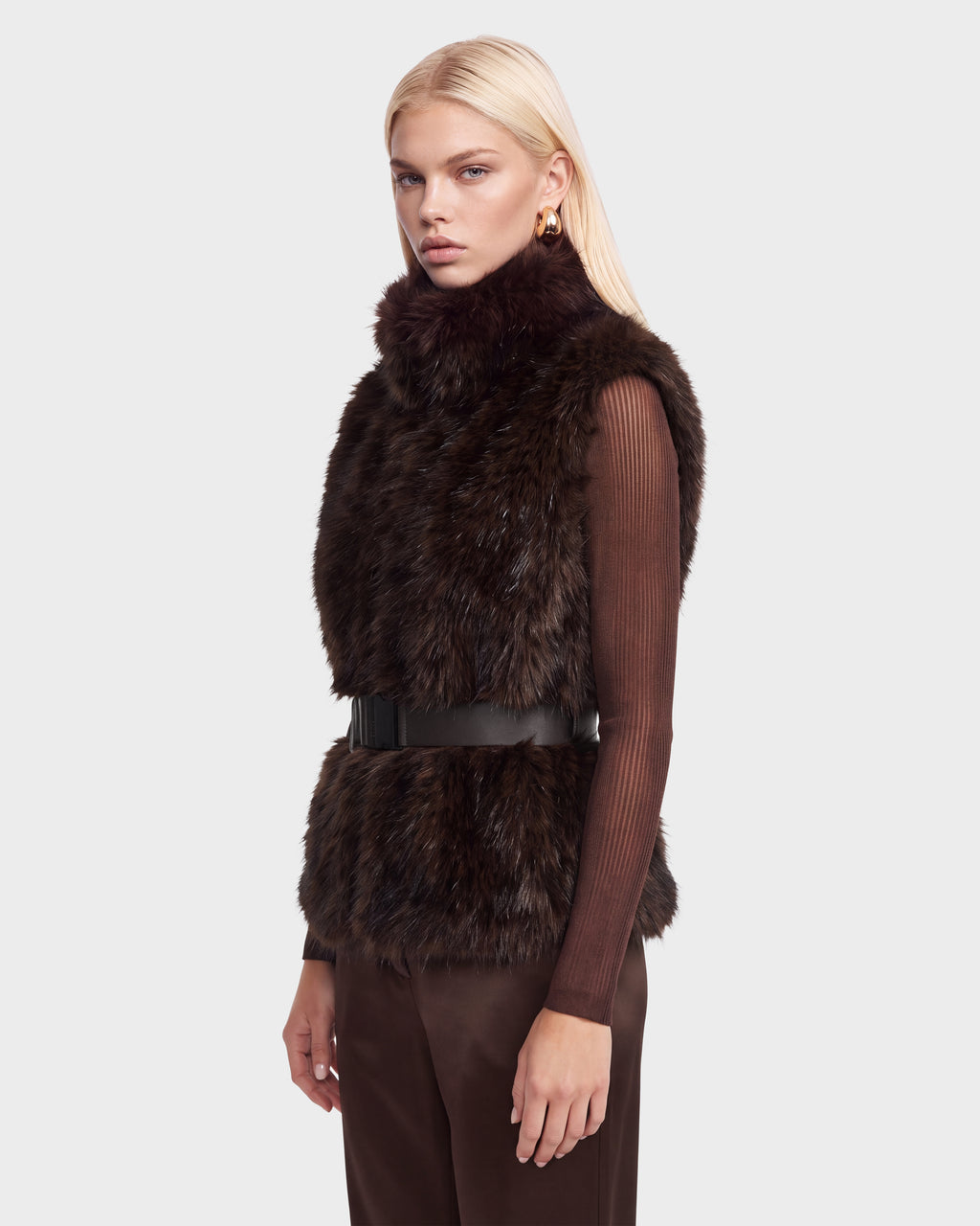 A sleeveless brown faux-fur MAULIN - 8524611 Mix Espresso vest worn over a sheer mock-neck pullover, cinched at the waist with a black vegan leather belt.