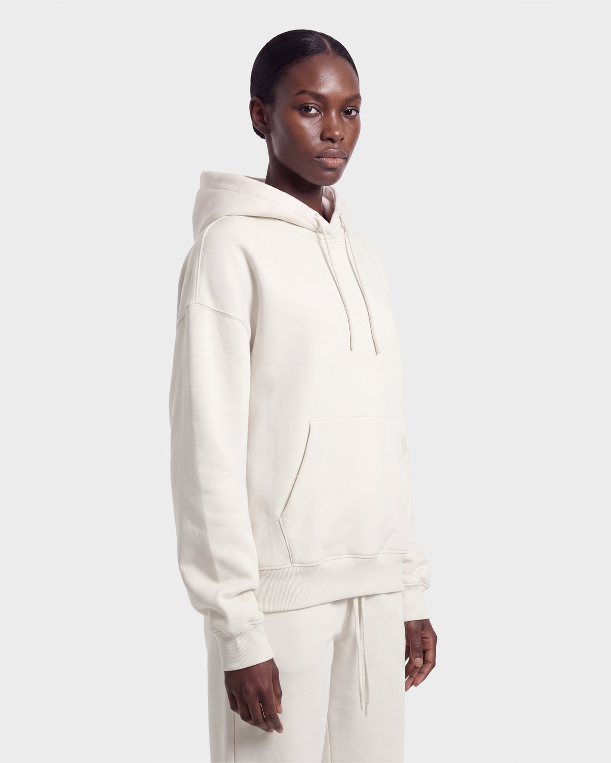 A person stands against a plain background wearing the Rudsak MILENA - 8526689 Vanilla hoodie and matching pants, with short, slicked-back hair and a neutral expression, looking slightly to the side.