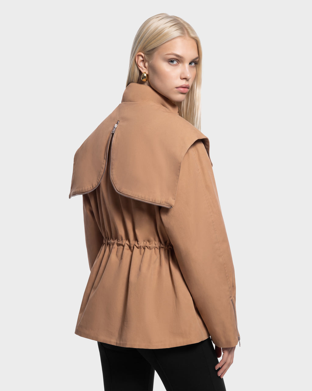 A woman wears a camel-colored ROSALINDA - 8126523 Camel jacket with a large back collar and cinched waist as she looks over her shoulder.