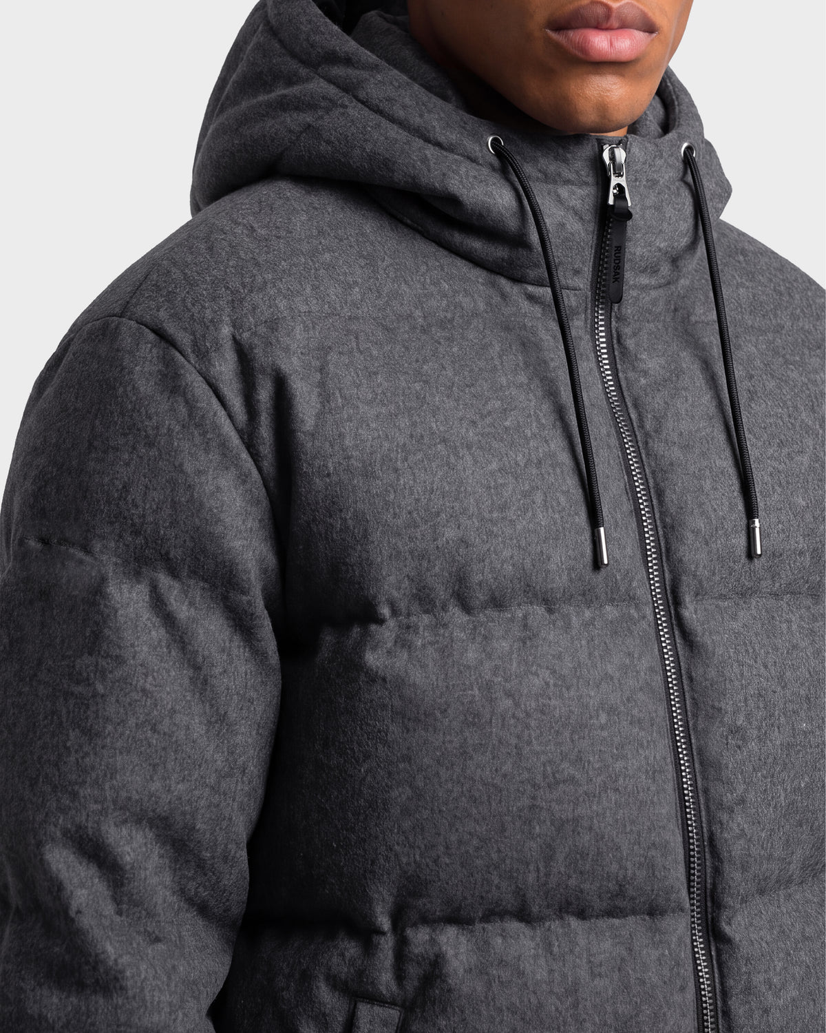 A person wearing the Rudsak STERLING W - 6126760 Heather Charcoal puffer jacket with a hood and drawstrings. The jacket is zipped up, and only the lower half of the person’s face and upper torso are visible.