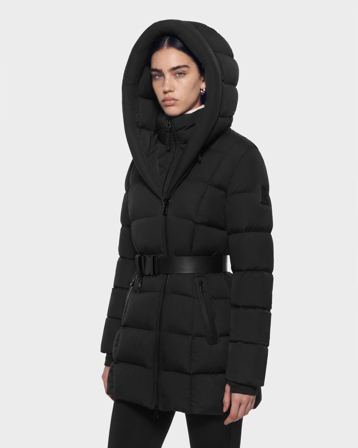 A person wearing a black Rudsak TAYLOR M - 8125965 Black puffer coat with a large hood and a waist belt.