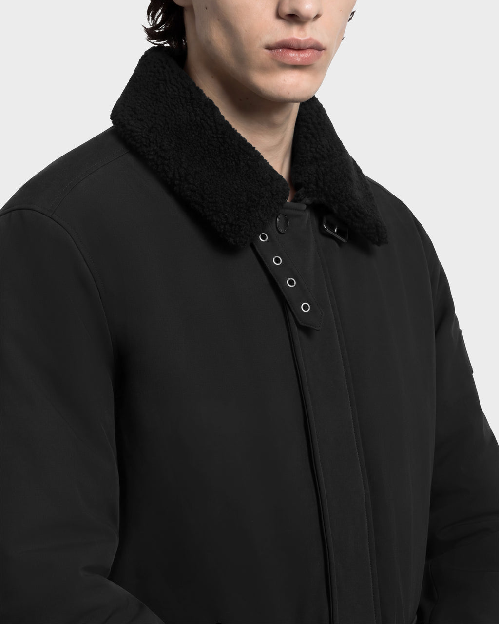 A person wearing a Rudsak ANTOINE - 6126506 Black refined utility jacket with a black faux-fur collar and a snap-button closure tab at the neck.