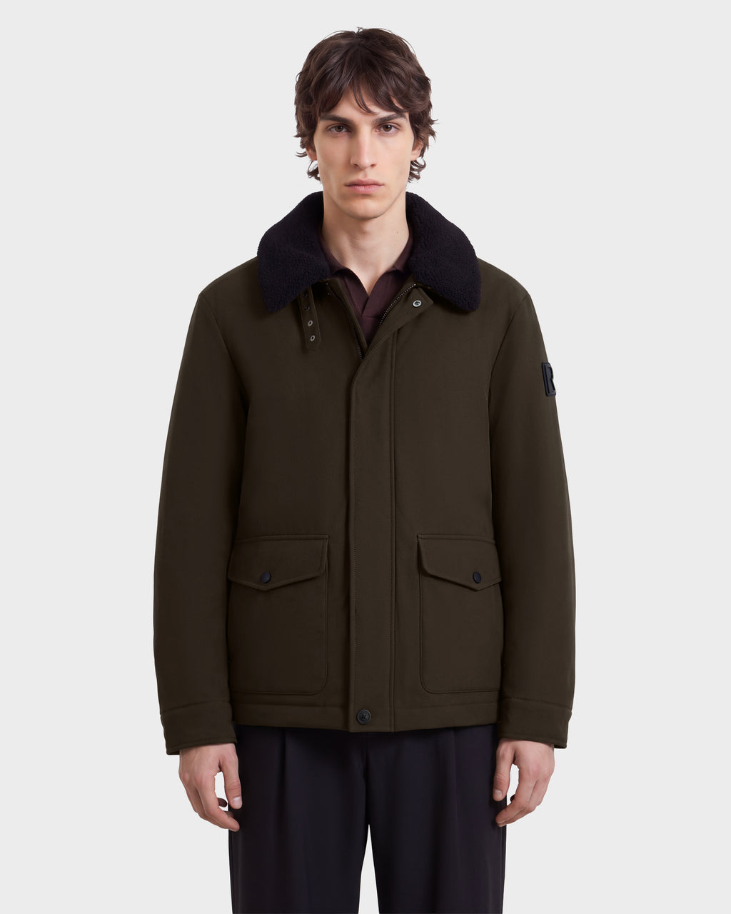 A man wears an olive green Rudsak ANTOINE - 6126506 Olive jacket with a dark faux-shearling collar and two large flap pockets.