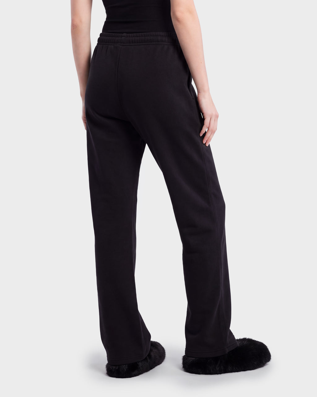 A person seen from behind wearing ANGEL - 8526725 Black contemporary sweatpants and black fuzzy slip-on shoes.