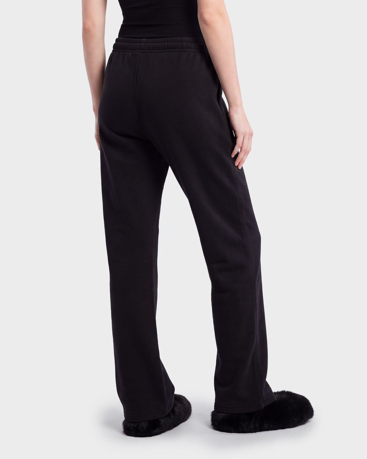A person seen from behind wearing ANGEL - 8526725 Black contemporary sweatpants and black fuzzy slip-on shoes.