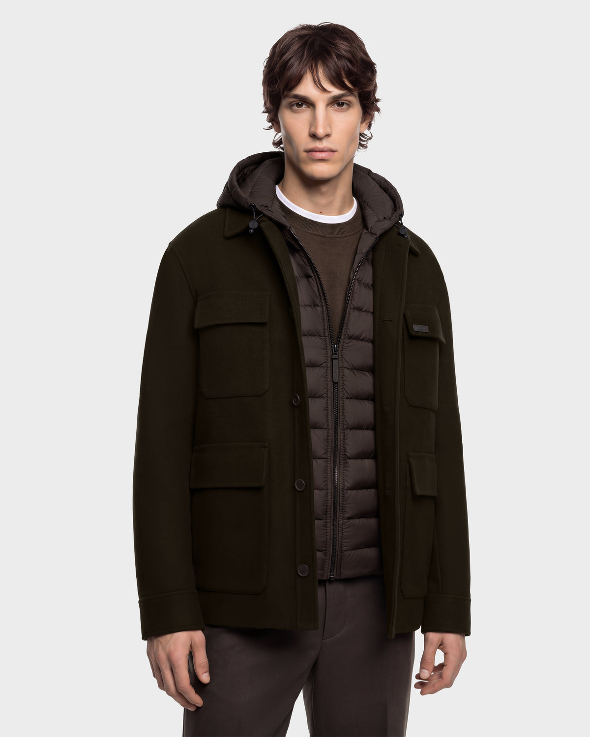A man wears a BRUNO - 6126716 Espresso dark brown hooded jacket layered over a quilted zip-up vest and a crew-neck shirt.