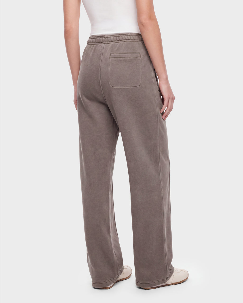 A person wearing the Rudsak GAELLE HV - H526902 heavyweight jersey jogger sweatpants in taupe, featuring an elastic waistband and a single back pocket, styled with a white tank top and white shoes, stands against a plain background for a look reminiscent of classic Harvard apparel.