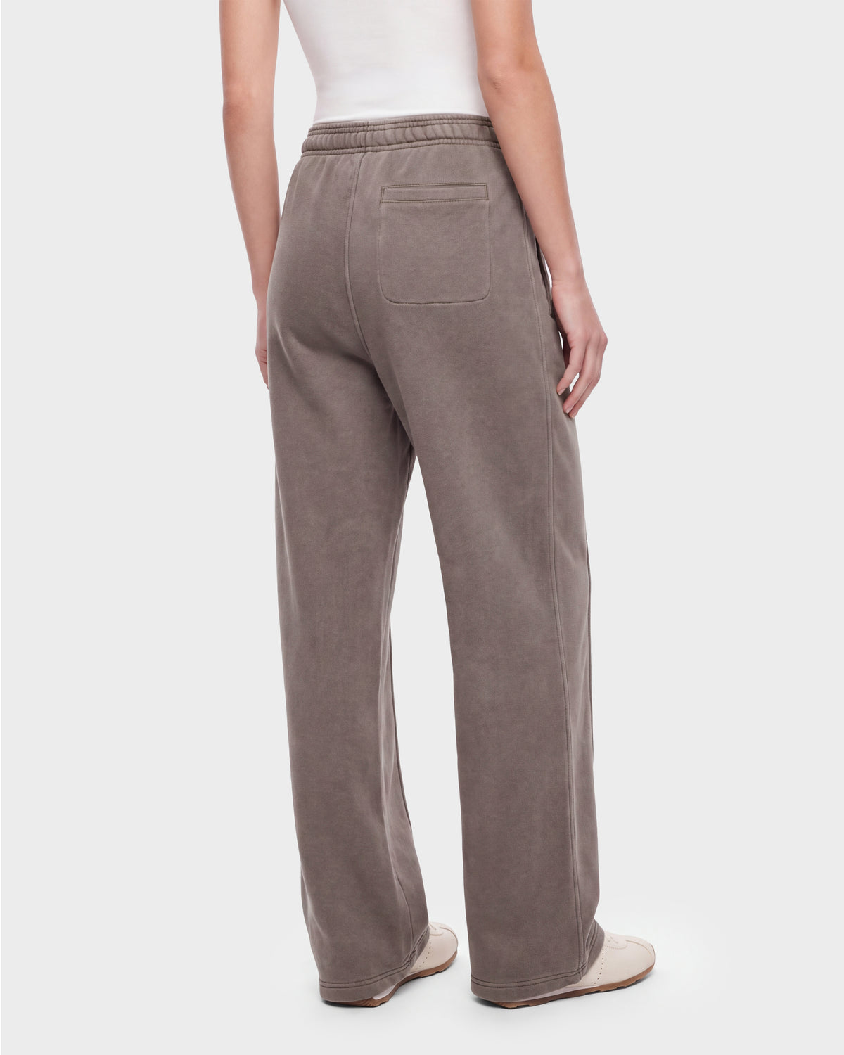 A person wearing the Rudsak GAELLE HV - H526902 heavyweight jersey jogger sweatpants in taupe, featuring an elastic waistband and a single back pocket, styled with a white tank top and white shoes, stands against a plain background for a look reminiscent of classic Harvard apparel.