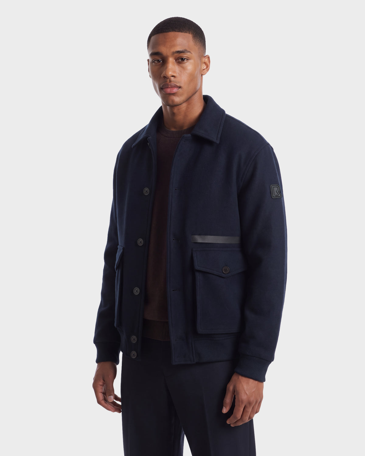 A man wearing a navy wool-blend JULIUS - 6126723 Navy jacket with a collar, button front, and large patch pockets.