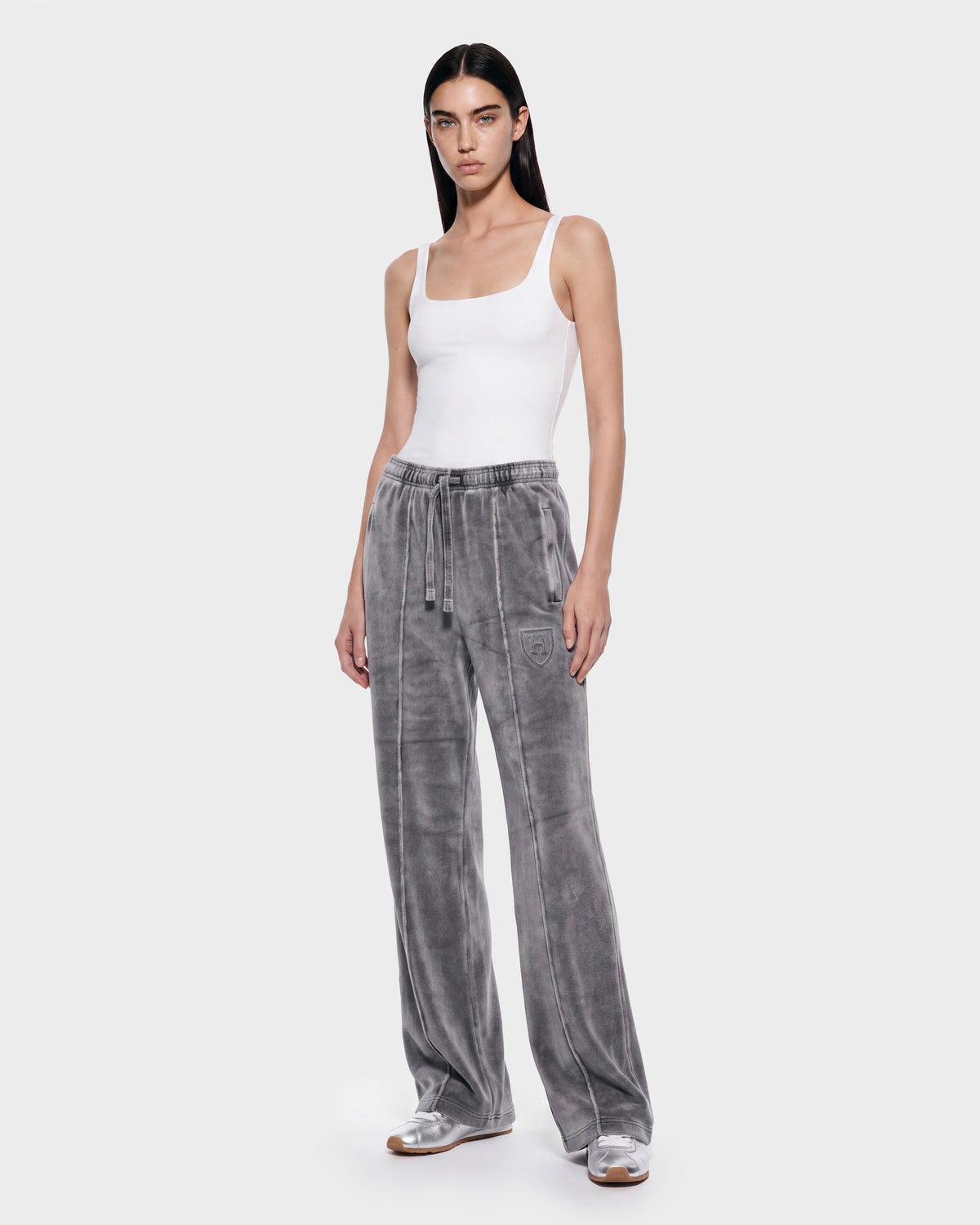 Wearing the OLIVYA HV - H526903 Titanium loose-fitting gray velvet sweatpants with drawstrings by Rudsak and a white tank top, a person stands against a plain light background.