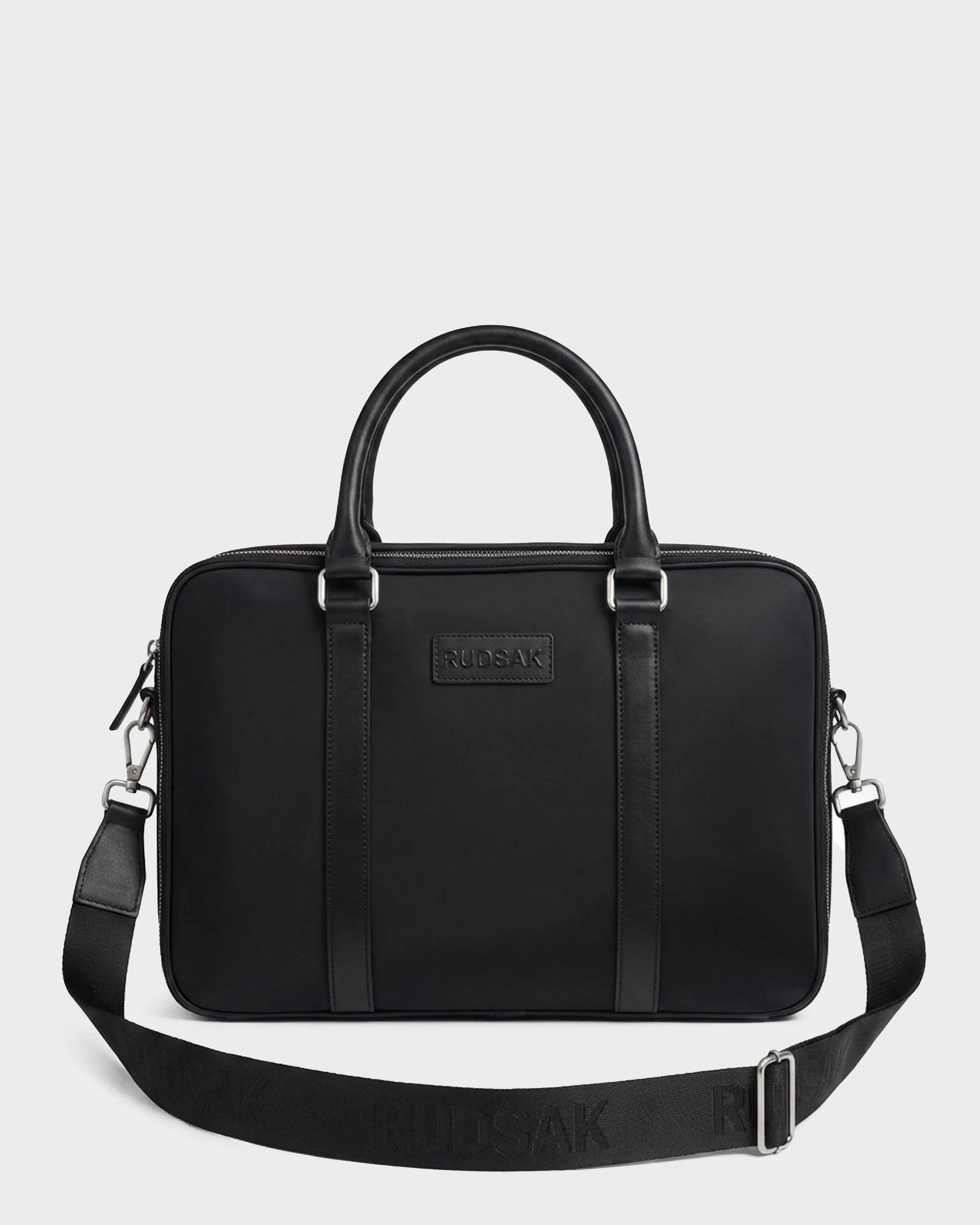 The Rudsak HENRY N - 9326056 Black laptop bag features a sleek, minimalist design with two handles, a detachable shoulder strap, and a front logo patch, shown against a plain white background.
