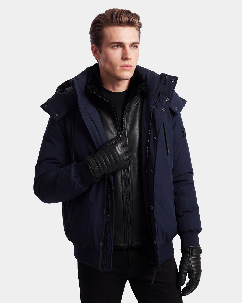 A man in the Rudsak WILL - 6126561 Navy bomber jacket and black leather gloves stands against a plain background, looking to the side. He wears a black shirt and a black zippered inner jacket.