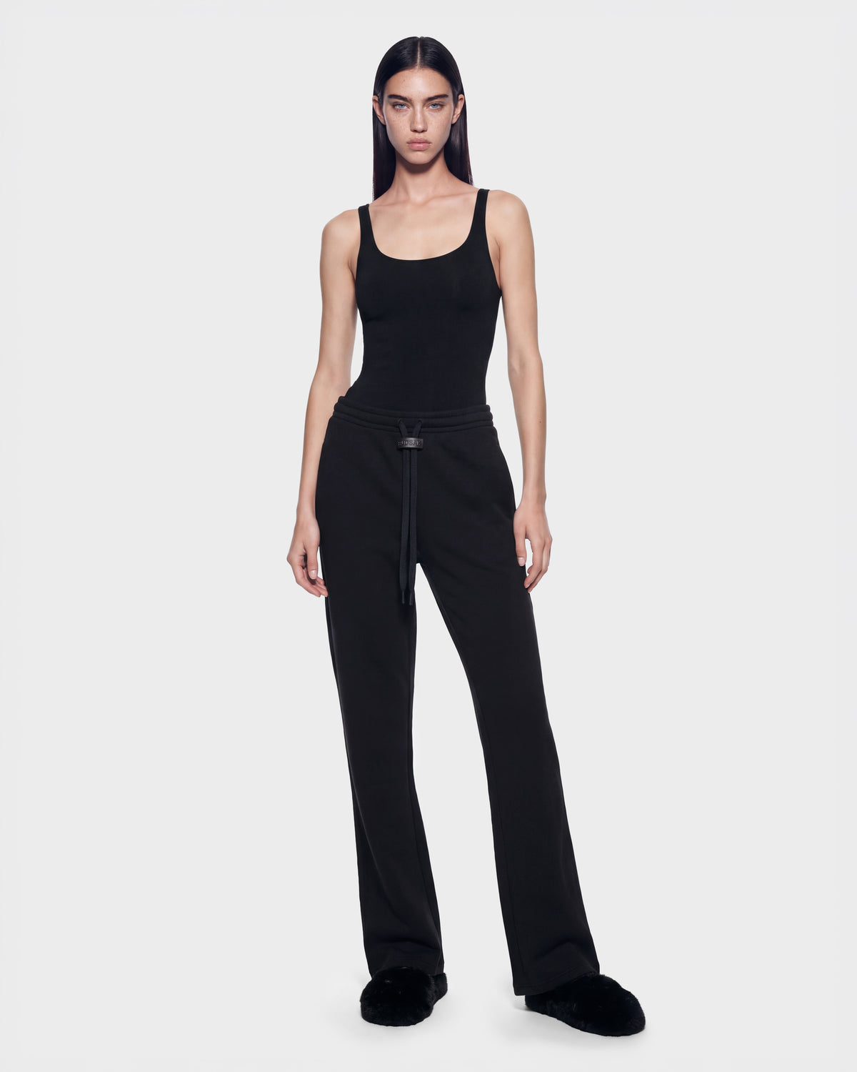 A person wearing an ANGEL - 8526725 Black scoop-neck tank top, contemporary black sweatpants with a drawstring waist, and black slippers for a refined off-duty look.