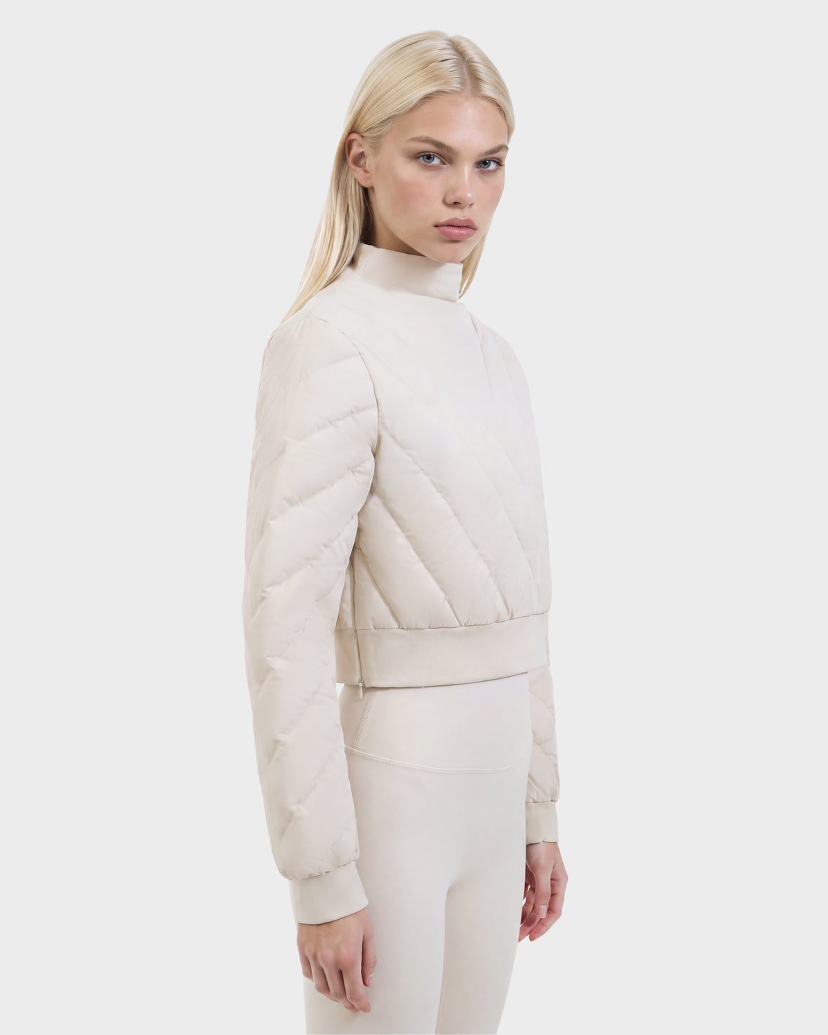 A person wears a KATYA - 8526531 Vanilla cropped down sweatshirt with a quilted design, high neck, and matching leggings.