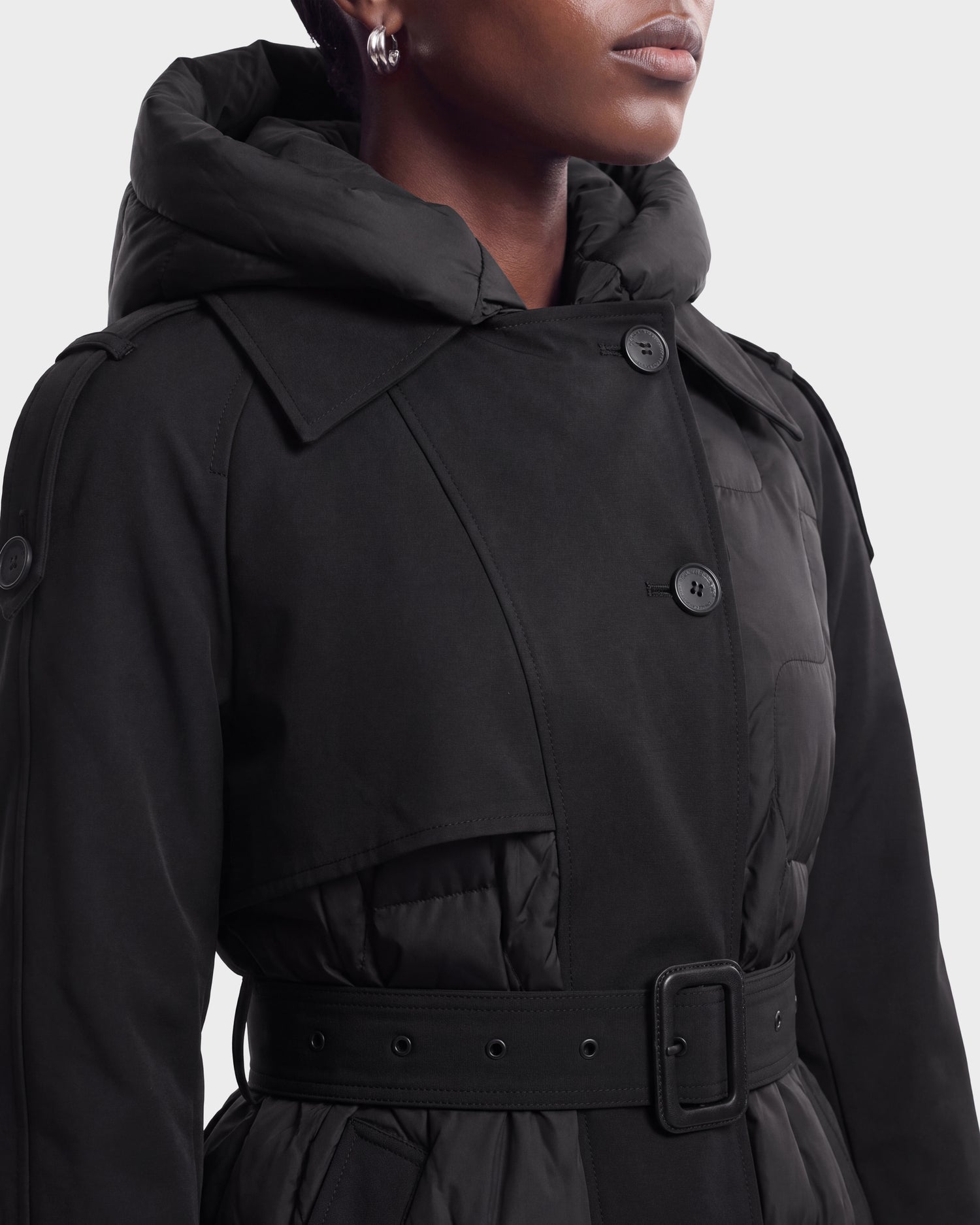 A woman wearing the Rudsak ELVIE - 8126512 black belted coat with a hood and button details, shown from the shoulders down against a plain background.