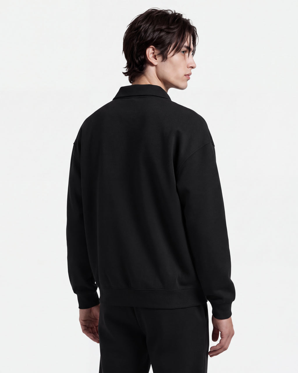 A person with dark hair stands facing away, wearing the Rudsak IDRIS - 6526500 Black long-sleeve polo collar sweater and relaxed black pants against a plain white background.