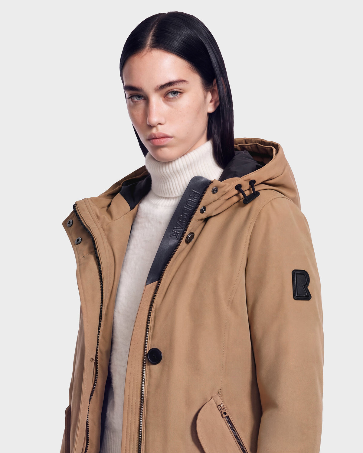 Woman with straight dark hair wears the Rudsak KEYSHIA - 8126517 Camel coat over a white turtleneck, looking forward with a neutral expression against a plain light background.