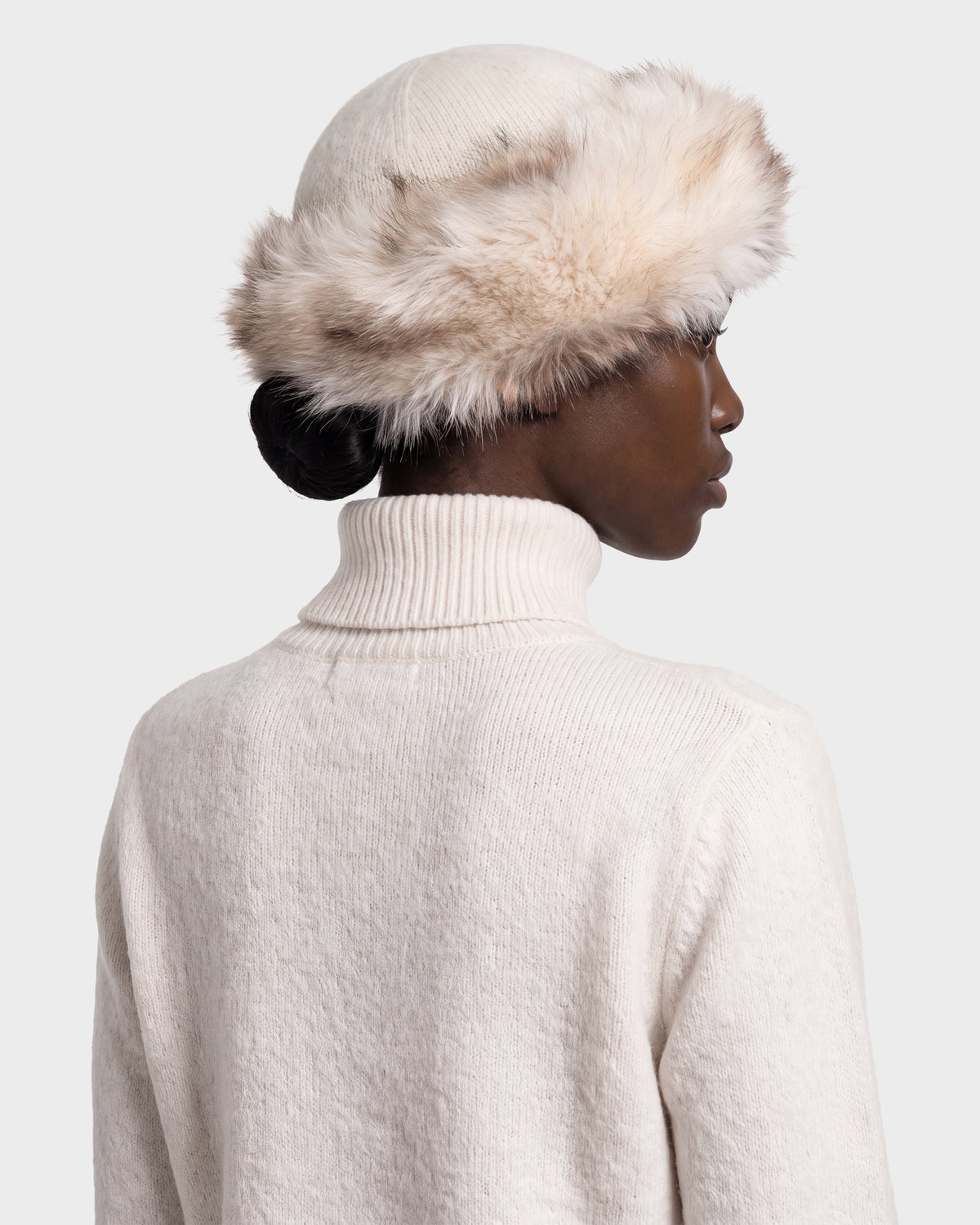 A person wearing a cream-colored Rudsak LORETTA W - 8426510 Vanilla faux fur hat with a wide, fluffy trim and a matching turtleneck sweater.