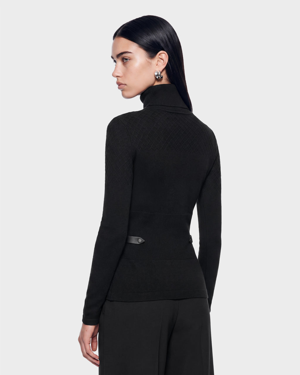 A person wearing a black Rudsak LAURA - 8524596 knit turtleneck sweater featuring quilted shoulder details, vegan leather trim, and a belted waistline.
