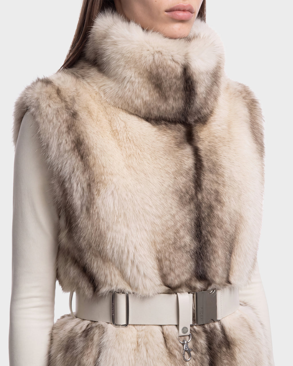 A person wearing a Rudsak MAULIN - 8524611 Mix Vanilla faux fur vest in cream and grey, featuring a high collar and a white belted waist.