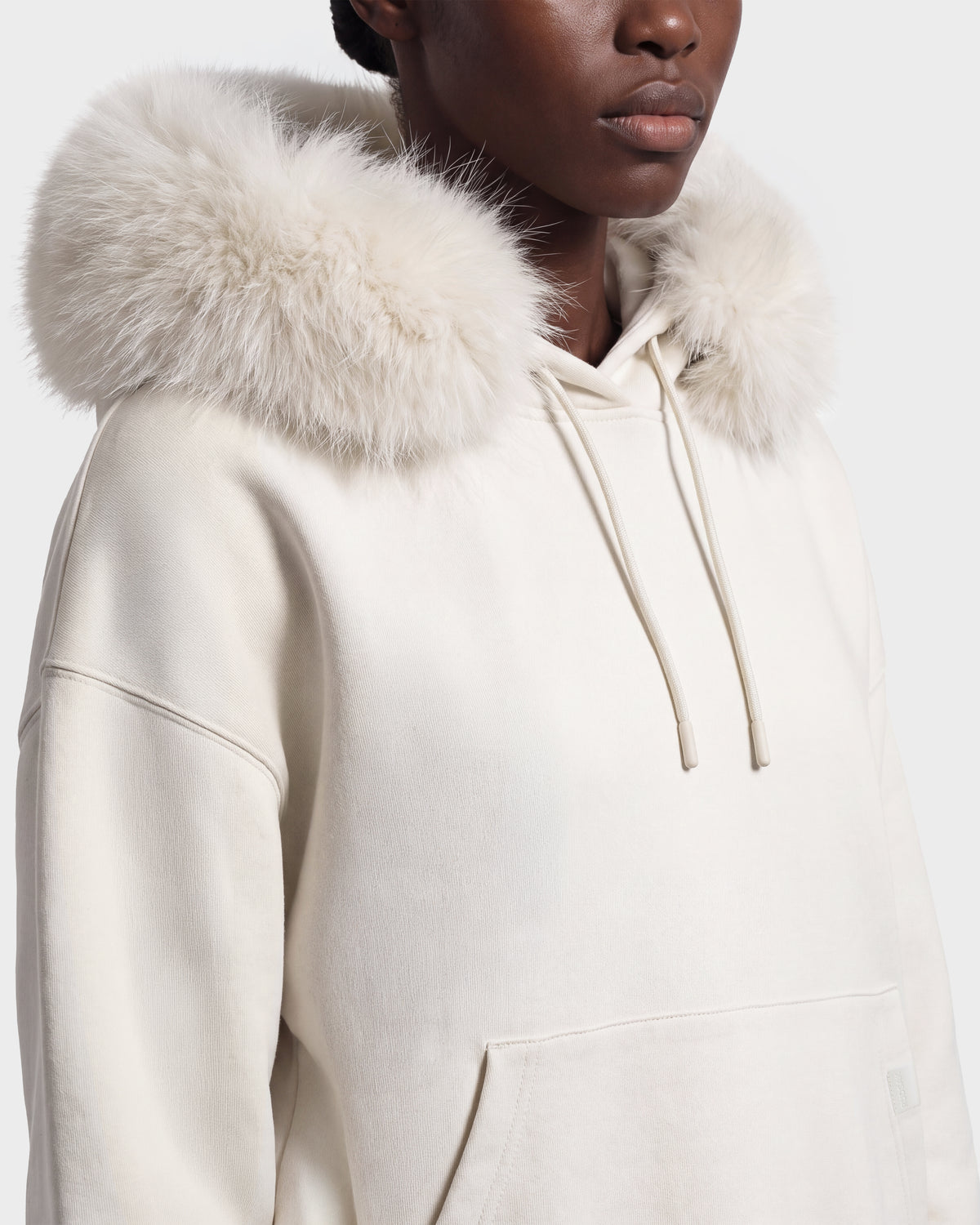 Wearing the MILENA - 8526689 Vanilla by Rudsak, a person’s lower face and upper body are visible, showcasing the off-white hoodie with a large, fluffy fur-trimmed hood.