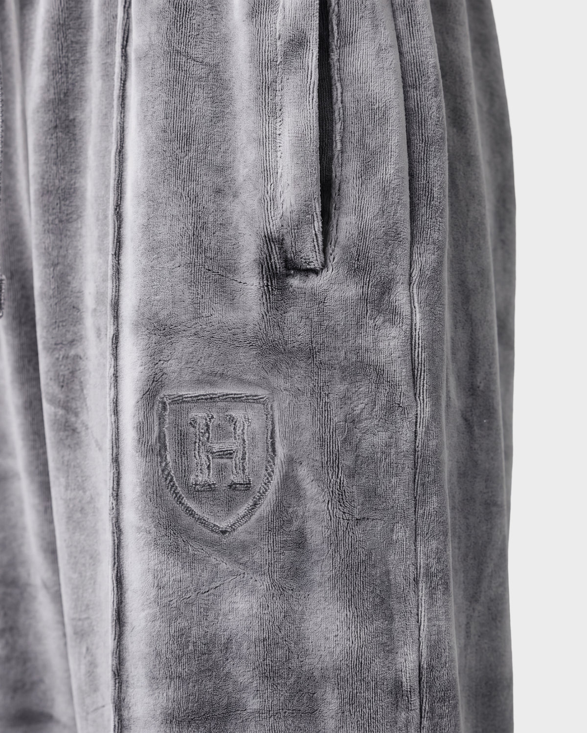 Close-up of the Rudsak OLIVYA HV - H526903 Titanium gray velour pants featuring a side pocket and an embossed shield emblem with the letter H on the upper thigh.