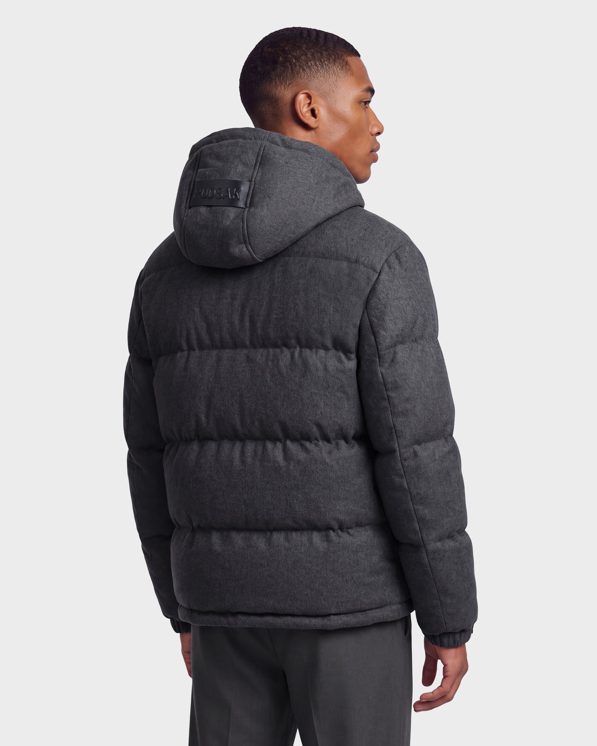 A person is shown from the back against a plain light background, wearing the Rudsak STERLING W - 6126760 puffer jacket in Heather Charcoal, featuring a hood.